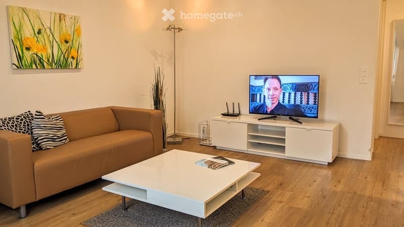 Modern living room with a brown leather sofa, white coffee table, TV stand, floor lamp, and a painting on the wall.
