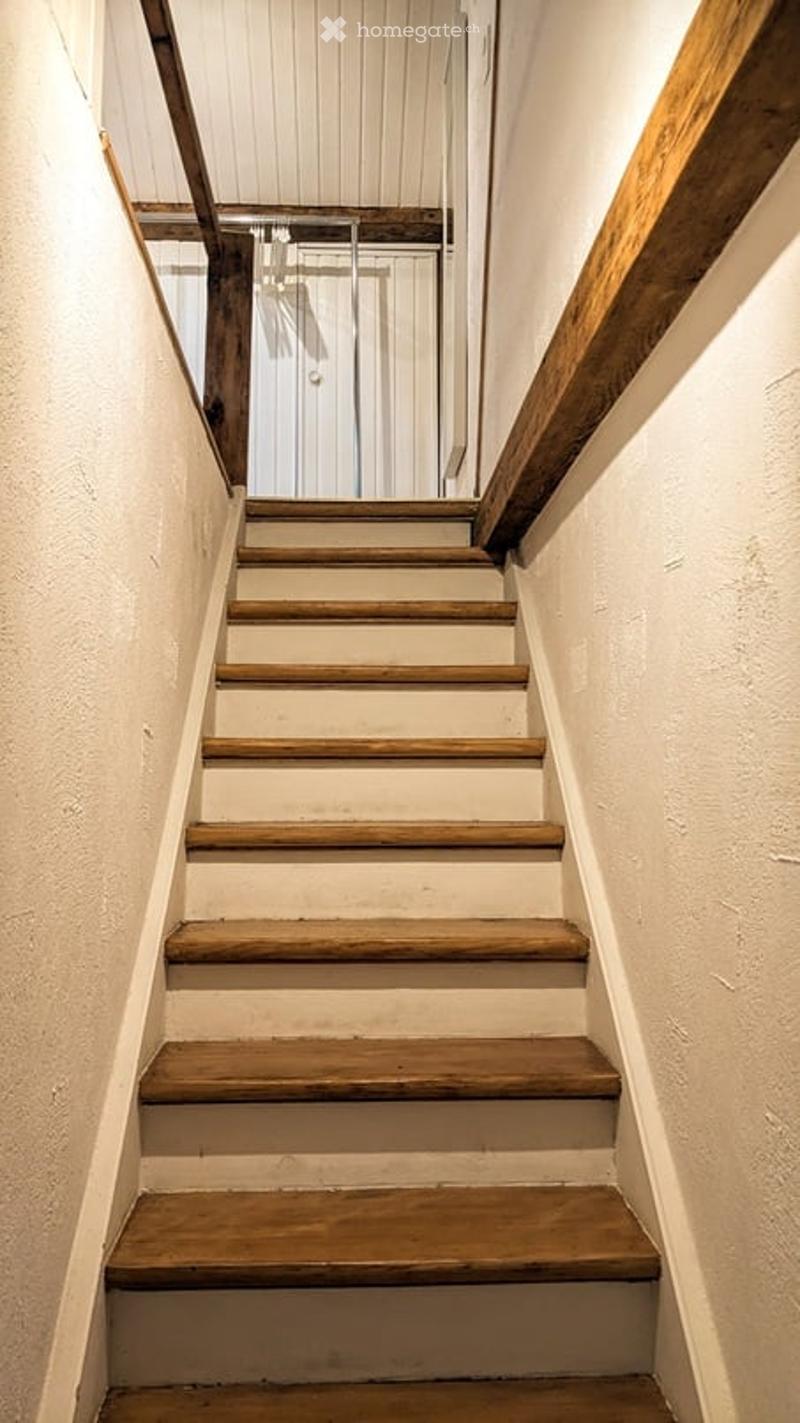 Wooden staircase with white walls and a wooden handrail, leading to an open area with a glass door at the end.