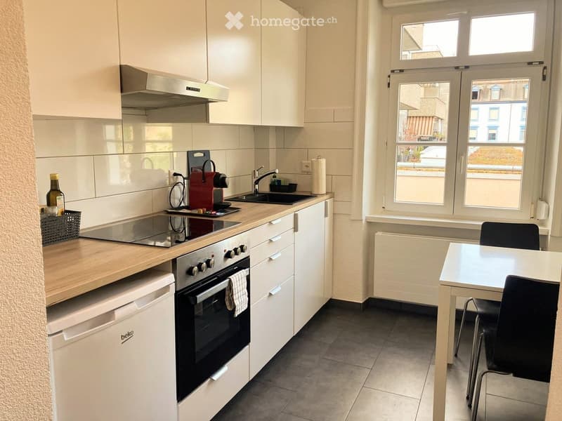 Modern kitchen with white cabinets, stainless steel appliances, and a small dining area with a table and chairs.
