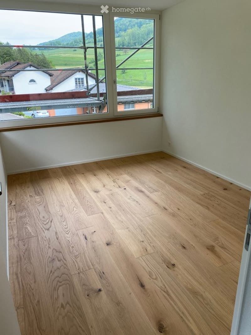 Empty room with wooden flooring and large windows offering a scenic view of the countryside and mountains.