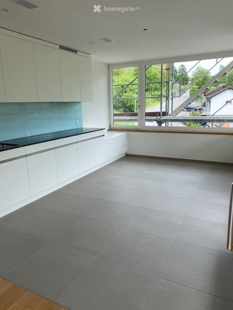 Modern kitchen with white cabinets, grey tiled floor, and large windows overlooking the outside.