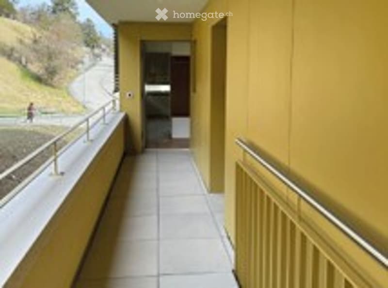 Balcony with yellow walls, white tiled floor, metal railings, and a view of a hillside.