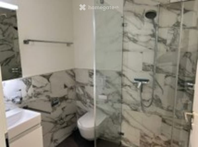 Modern bathroom with marble tiles, a glass-enclosed shower, a toilet, and a sink.