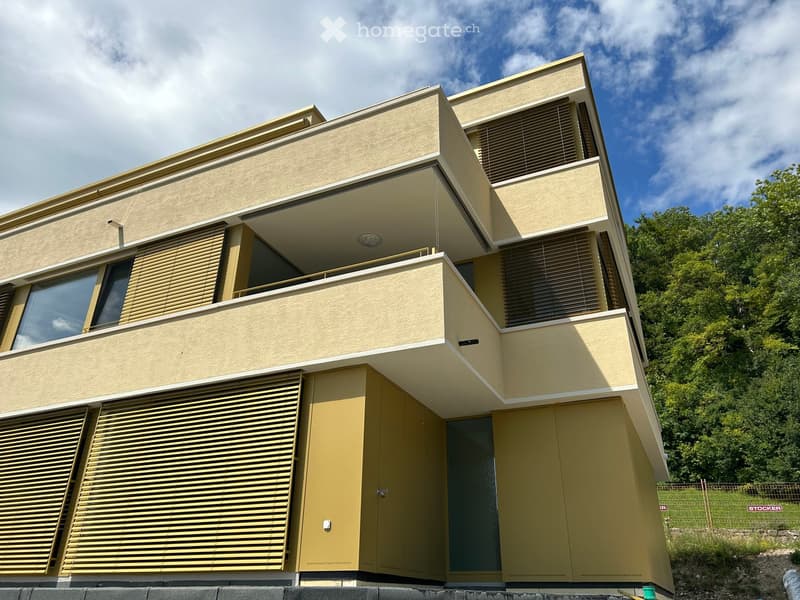 Modern three-story building with beige facade, large windows, and balconies. Features contemporary design with clean lines and a raised ground floor.