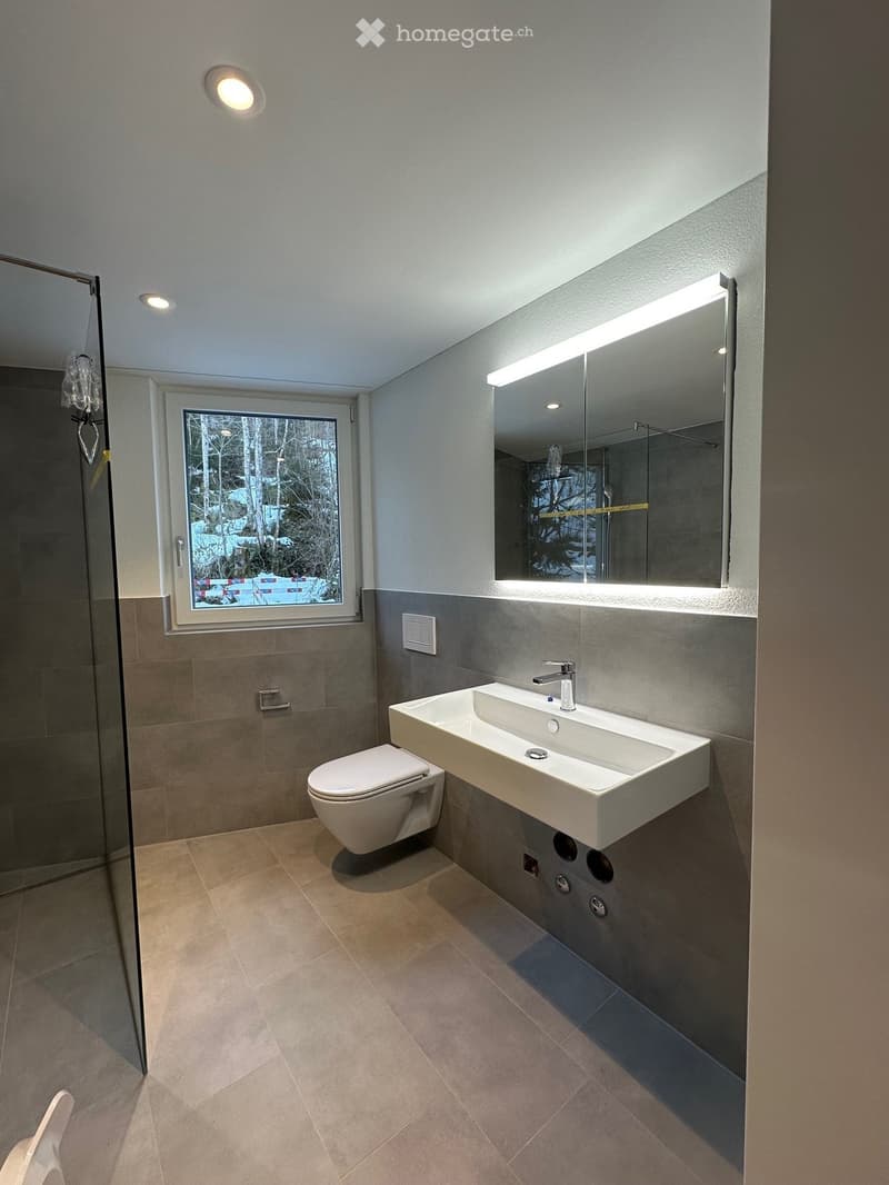 Modern bathroom with a white sink, toilet, large mirror with LED lighting, and a glass-enclosed shower area.