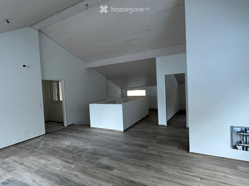 Empty room with wooden flooring, white walls, and a raised ceiling. Features include a doorway leading to another room and a small window letting in natural light.