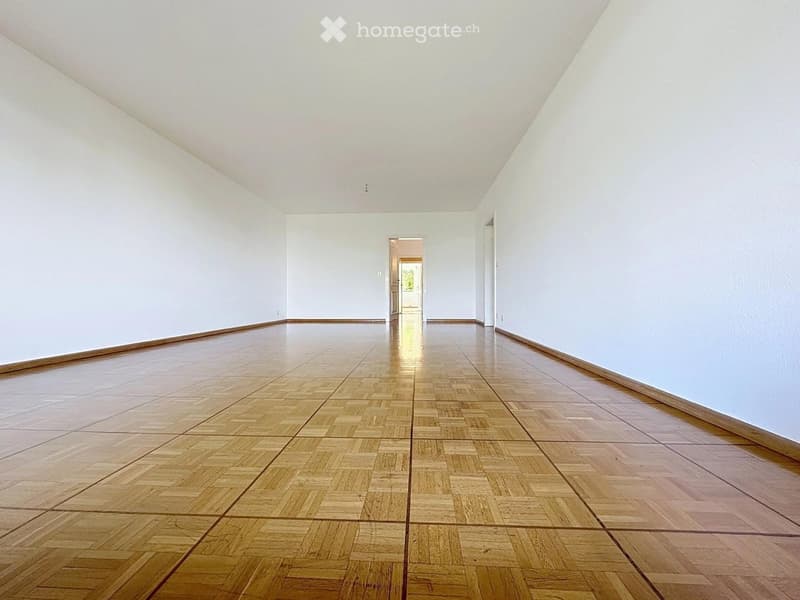 Empty room with light-colored walls and a polished wooden floor, featuring a doorway leading to another space.