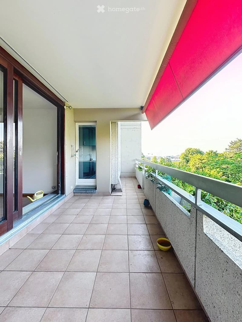 Balcony with tiled floor, white walls, and a red awning. Features a small enclosed area with a sink and a door leading to the interior.