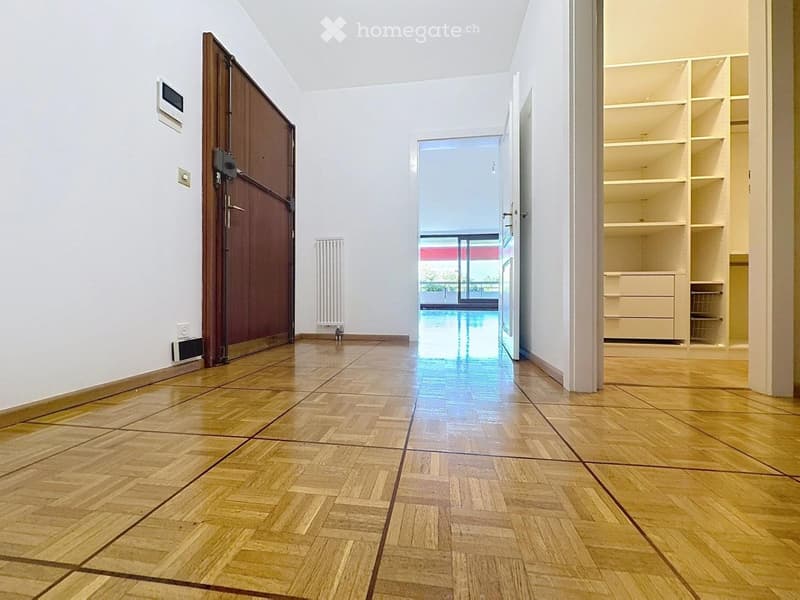 Empty hallway with wooden flooring, white walls, and a built-in closet with shelves. A door leads to an outdoor area with a pool visible through a large window.