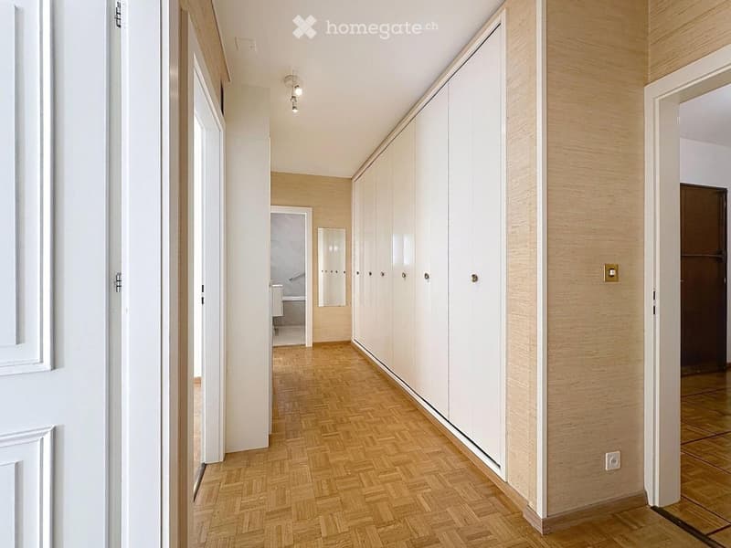 Clean, modern hallway with wooden herringbone flooring, white built-in wardrobes, and recessed lighting. Doors lead to other rooms.