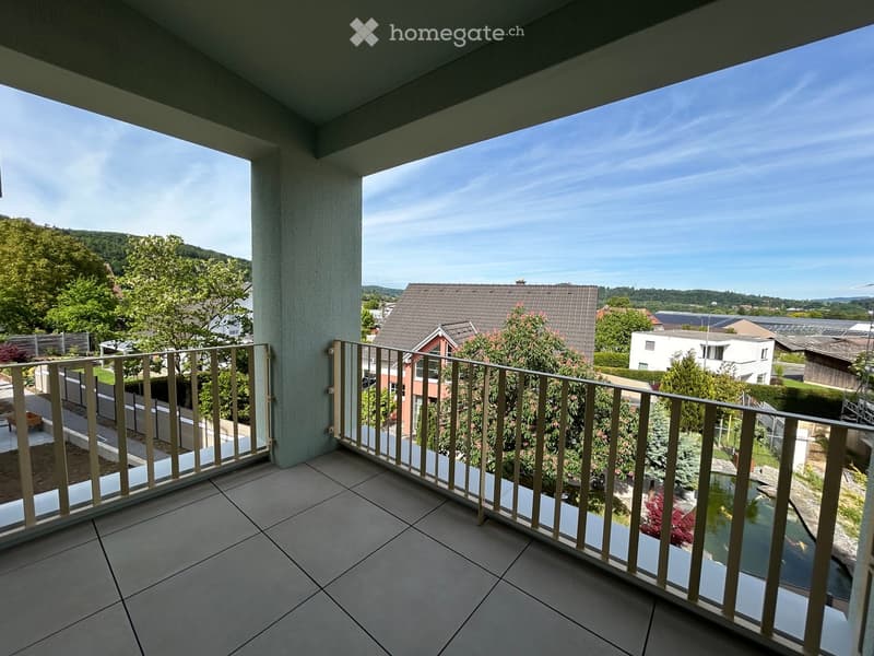 Balcony with tiled floor and metal railing, overlooking a residential area with houses, trees, and a pond.