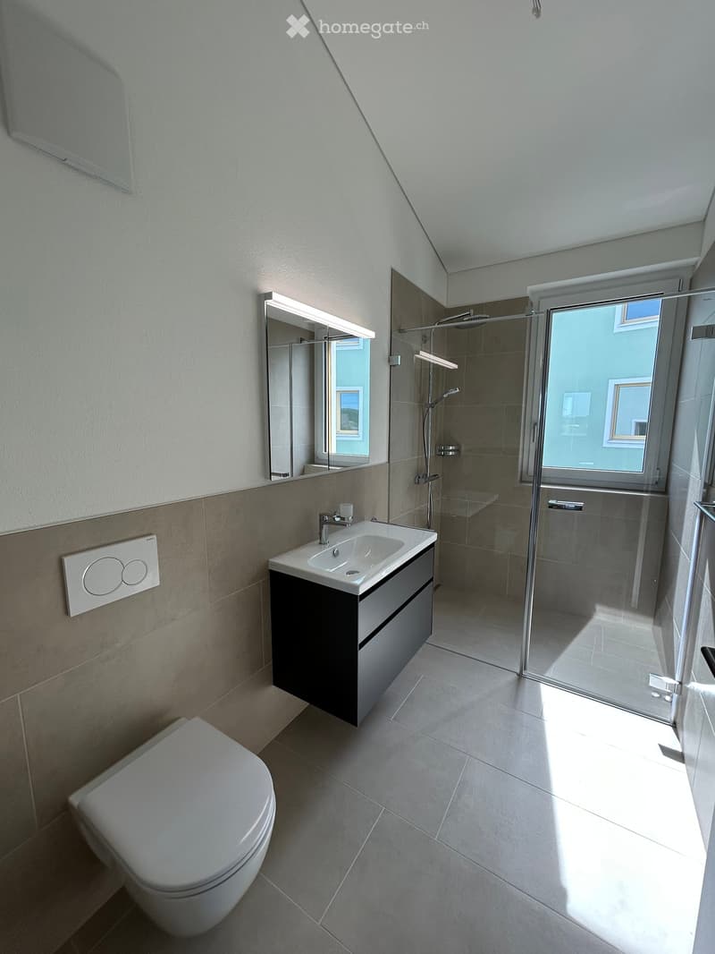Modern bathroom with a toilet, sink, mirror, and glass-enclosed shower. Light-colored tiles and a sleek design.