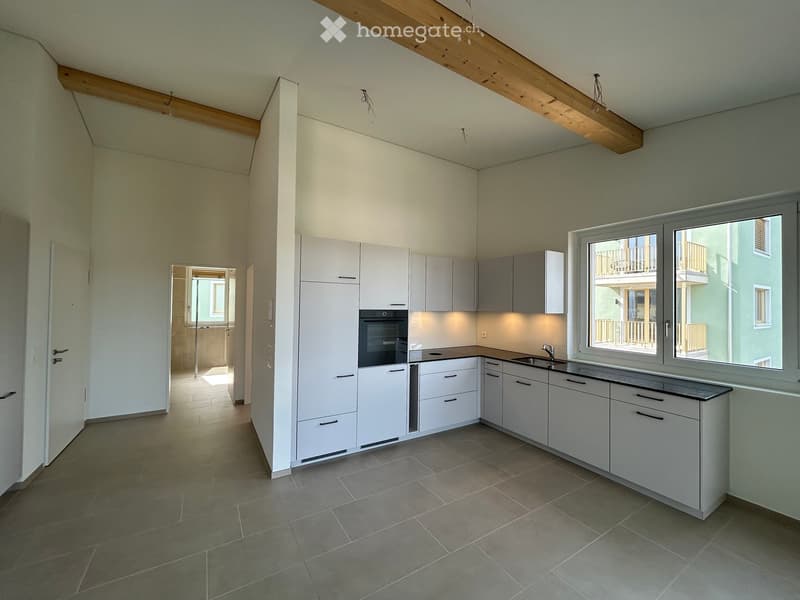 Modern kitchen with white cabinets, a sink, and an oven, featuring large windows and a view of a balcony.