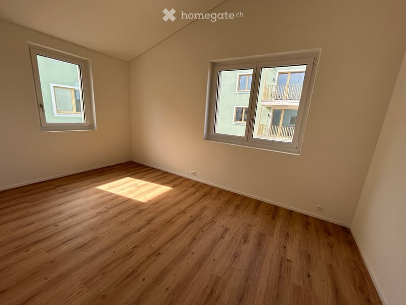 Empty room with wooden flooring and large windows, allowing natural light to enter.
