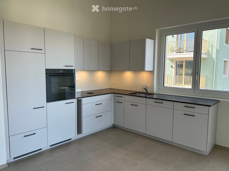 Modern kitchen with white cabinets, black countertops, and built-in appliances including an oven and sink.