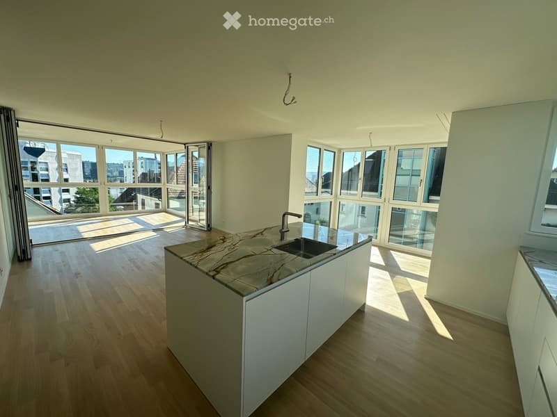 Modern kitchen with light wooden flooring, white cabinets, and a marble countertop. Large windows and sliding glass doors provide ample natural light and access to a balcony.