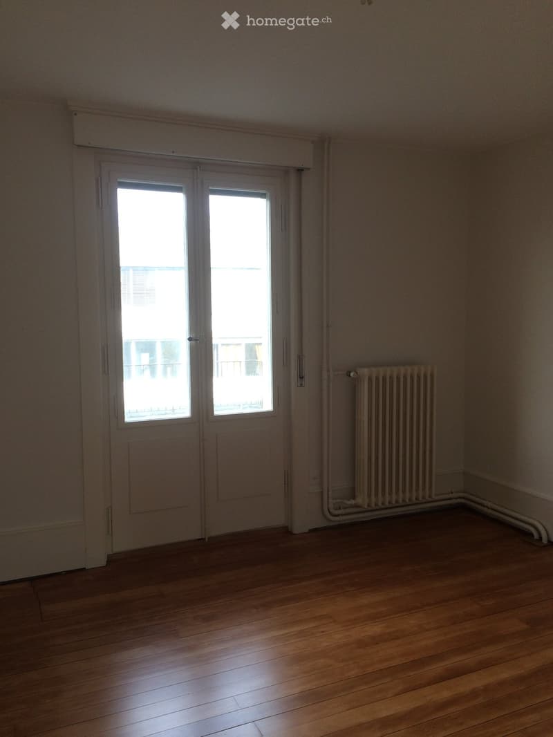 Empty room with wooden flooring, white walls, a radiator, and a large sliding glass door with a view of a balcony.