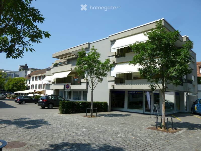 white multistory building with white awnings, parking area, trees, cars parked in front