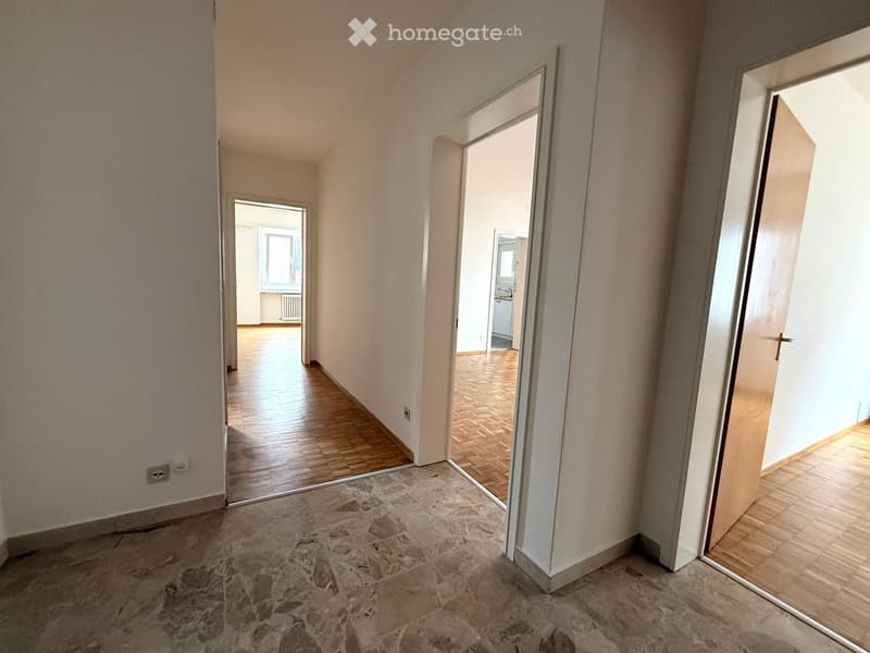 Empty hallway with wooden flooring, light-colored walls, and multiple open doors leading to other rooms.