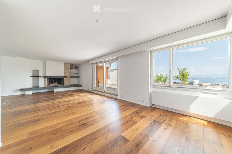 Empty living room with wooden flooring, large windows, fireplace, and sliding glass doors leading to a balcony.