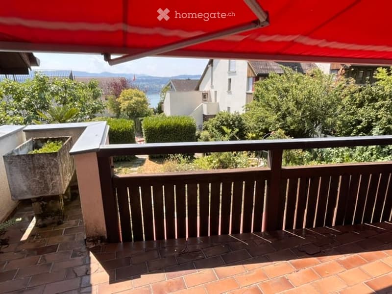 Balcony with wooden railing, brick tiles, and a view of a garden and distant hills.