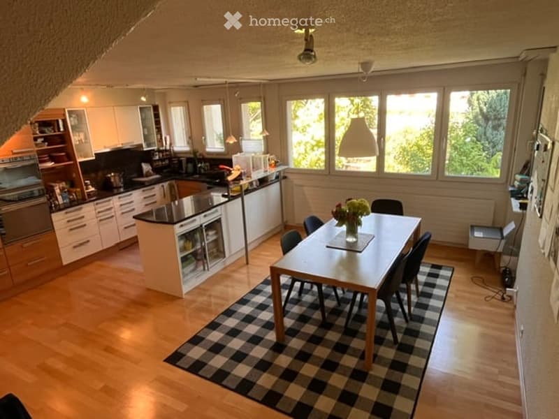 Bright, open-plan kitchen and dining area with wooden flooring, large windows, modern kitchen cabinets, a central island, and a dining table with chairs.