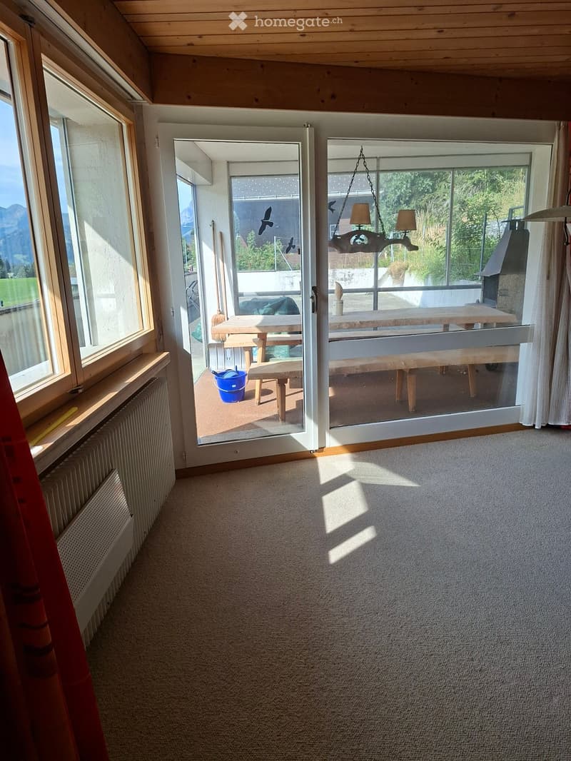 Bright hallway with carpeted floor, large windows, and sliding glass doors leading to a patio area with outdoor furniture.