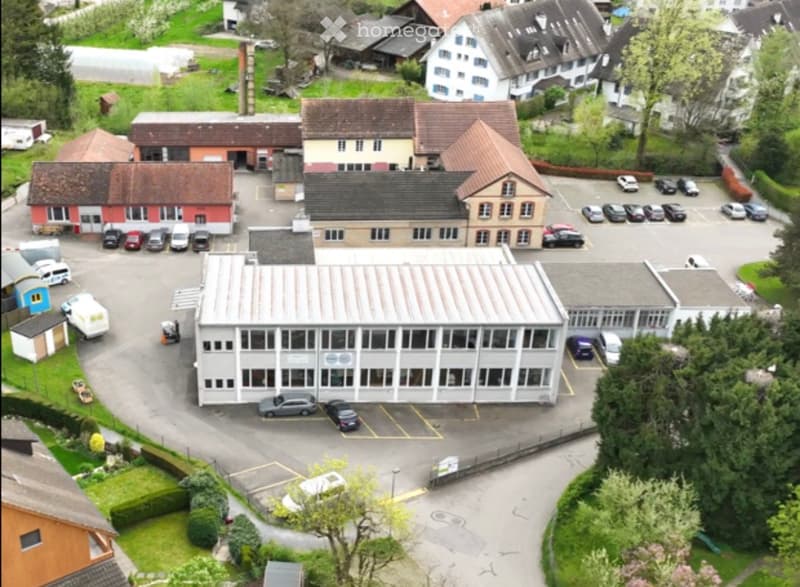 Aerial view of a multi-building complex with parking lot, surrounded by residential houses and greenery.