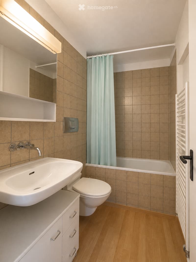 Modern bathroom with a white sink, chrome faucet, toilet, bathtub with a light blue shower curtain, a built-in mirror cabinet, and a white radiator.
