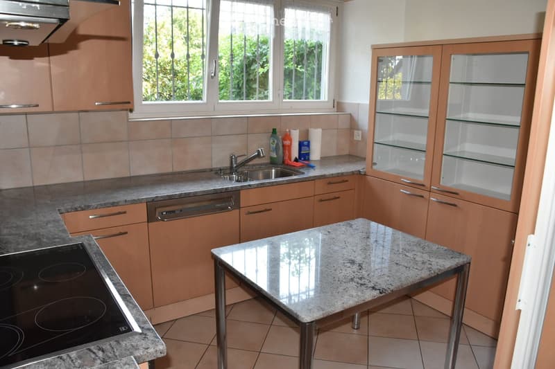 Modern kitchen with light wooden cabinets, granite countertops, a built-in stove, dishwasher, and a central island table.