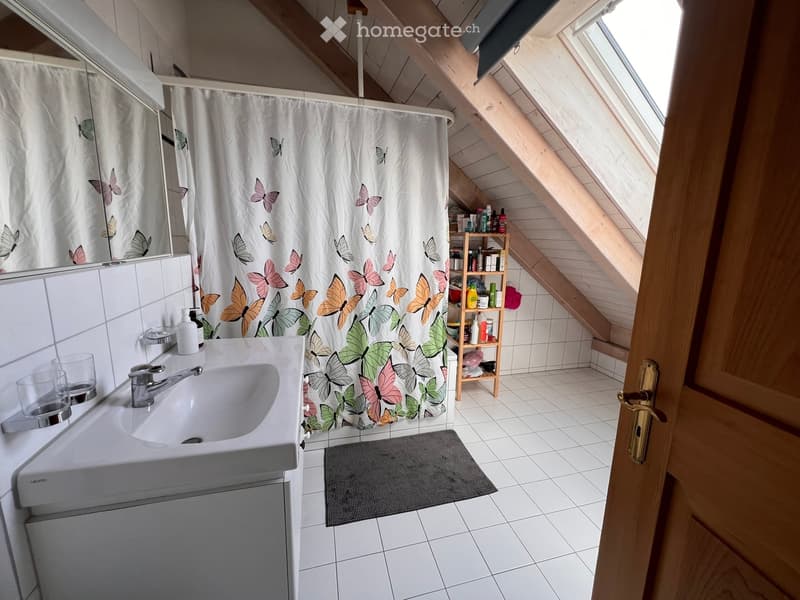 Bathroom with a white sink, mirror, shower curtain with butterfly design, and a small wooden shelf holding toiletries.