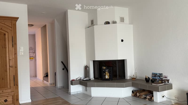 Modern living room with a white fireplace, grey tiled surround, wooden floor, and decorative items on the mantel.