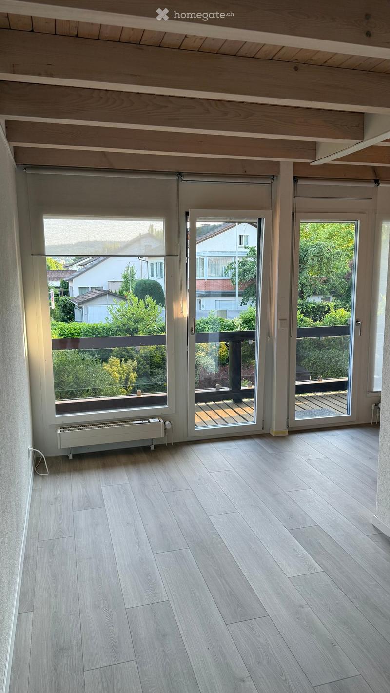 Empty room with light wooden flooring, large windows, and sliding glass doors leading to a balcony or terrace area.