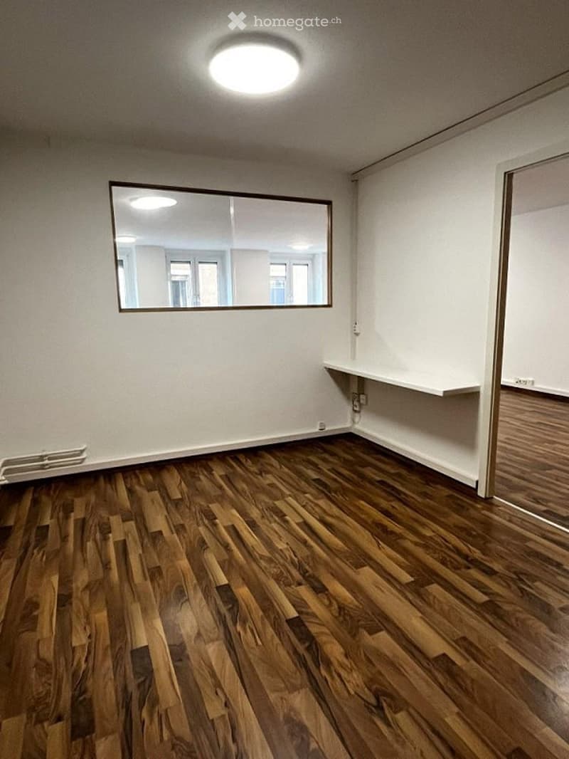 Empty room with wooden flooring, white walls, a large mirror, and a built-in shelf. No furniture or equipment present.