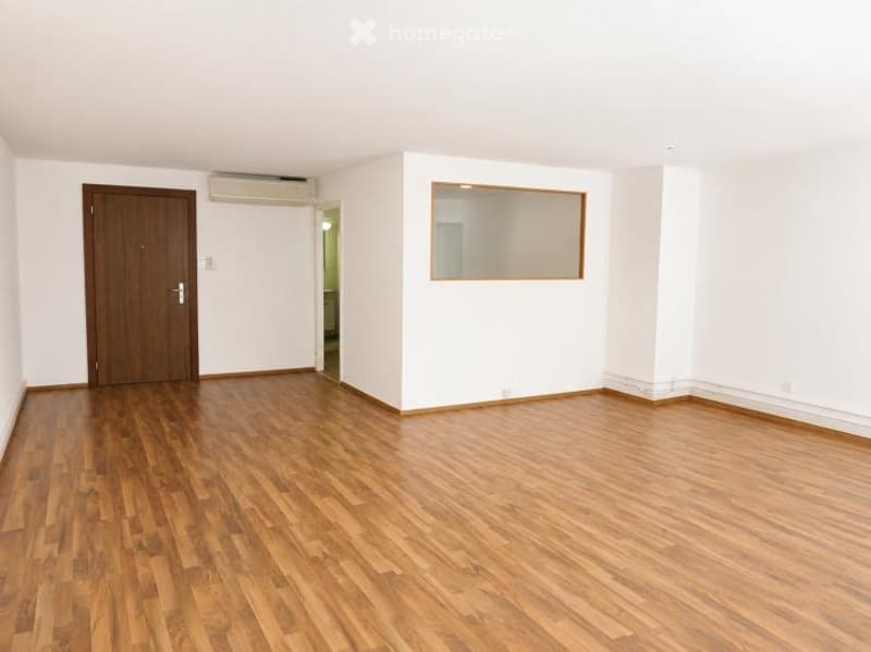 Empty room with wooden flooring, white walls, a wooden door, and a mirror on the wall.