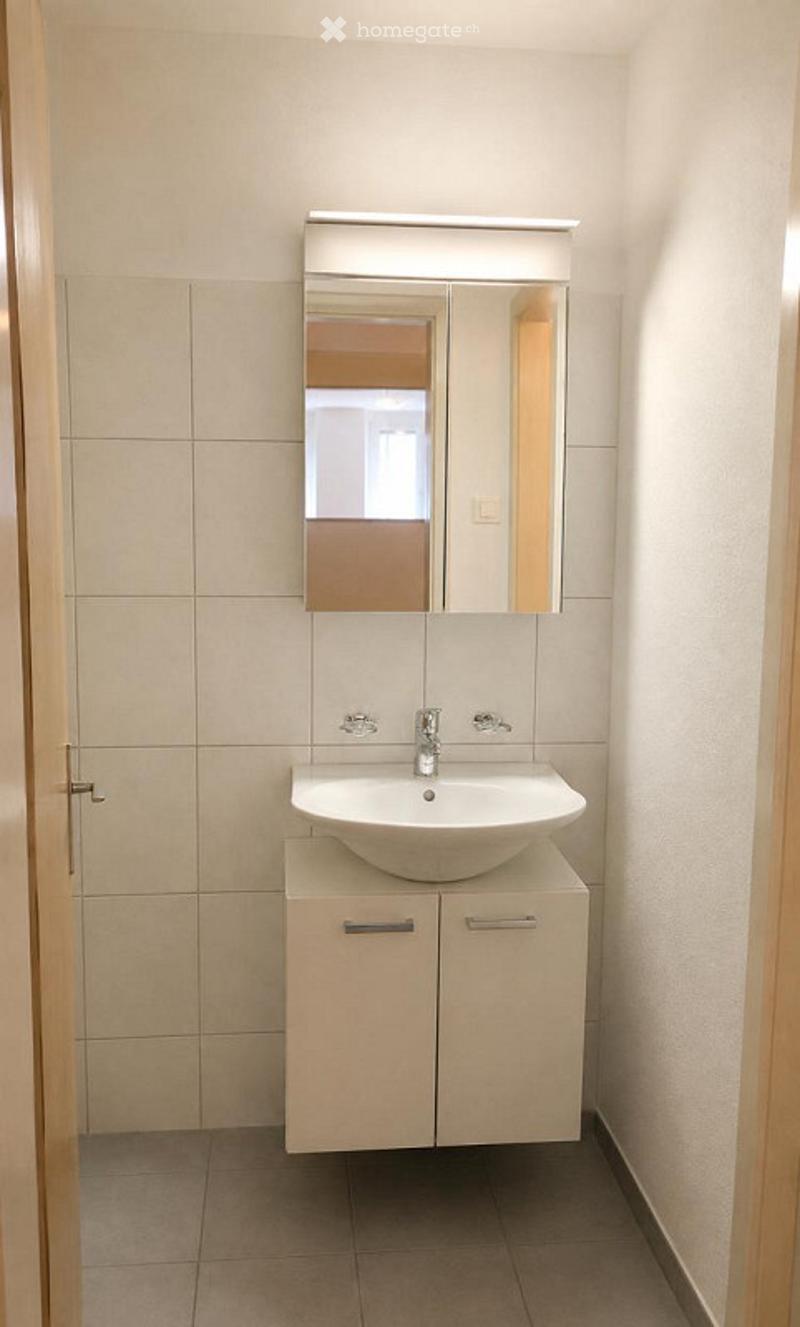 Modern bathroom with a white sink, mirrored cabinet, and tiled walls.