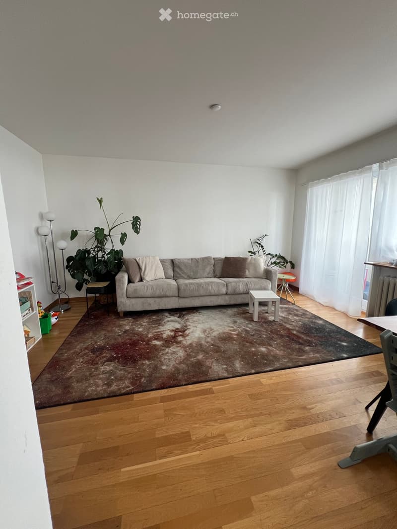 Living room with wooden flooring, large sofa, coffee table, side tables, floor lamp, and plants.