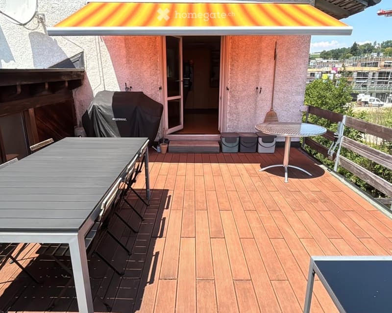 Wooden deck with a table, chairs, and a covered grill, with a view of the surrounding area.