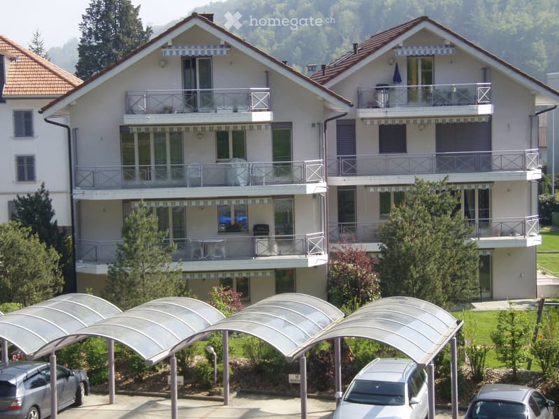 Two-story house with multiple balconies, covered parking area, and surrounding greenery.