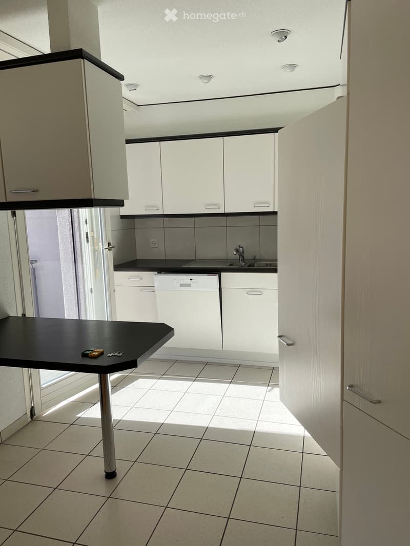 Modern kitchen with white cabinets, black countertops, a sink, a dishwasher, and a small black table with keys and a small device on it.