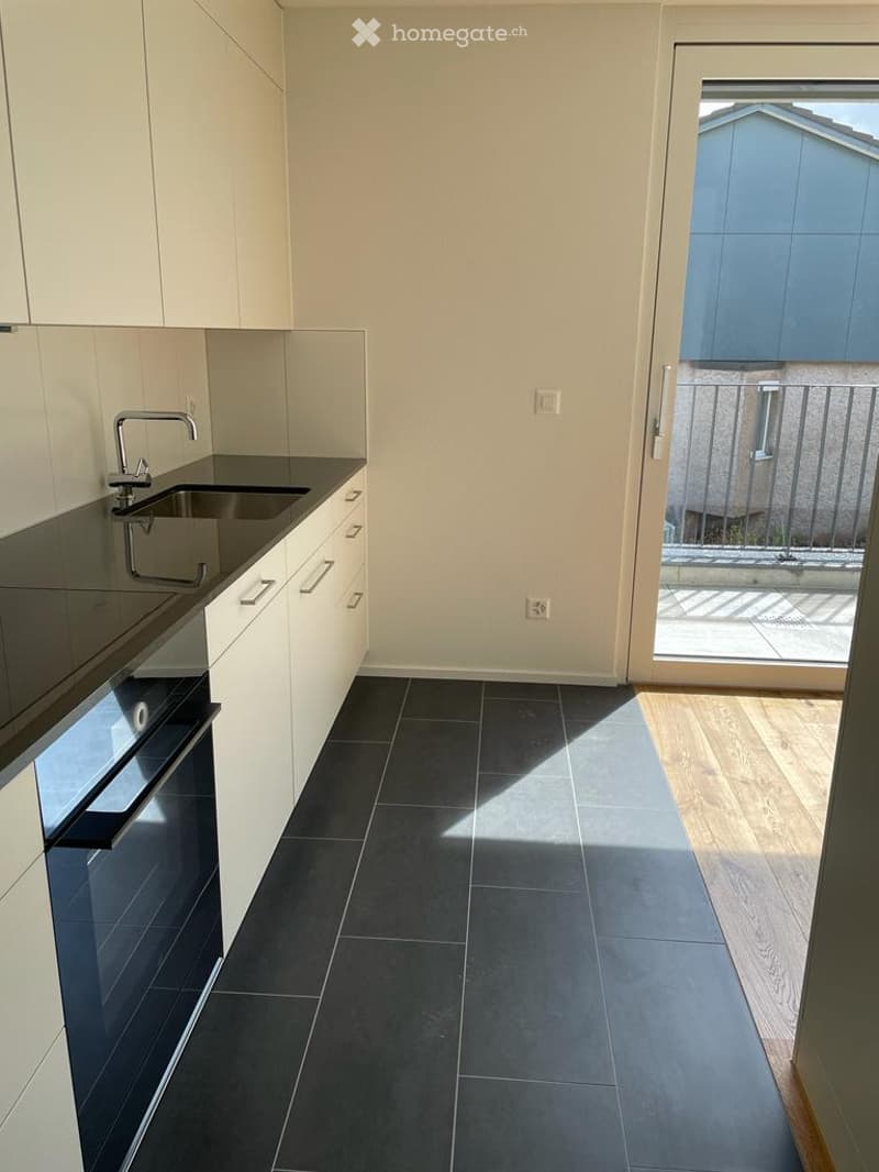 modern kitchen with black granite countertops, stainless steel faucet, white cabinetry, dark gray tiled flooring, glass door leading to balcony