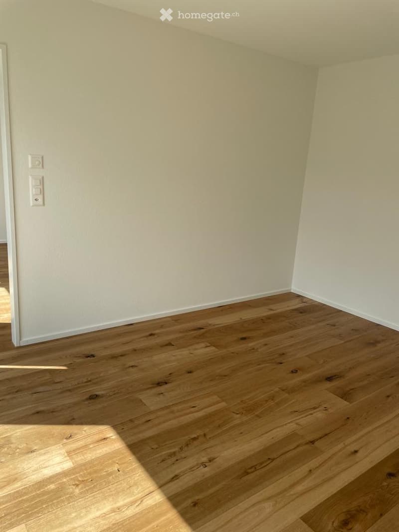 Empty room with wooden floor, white walls, and electrical outlets