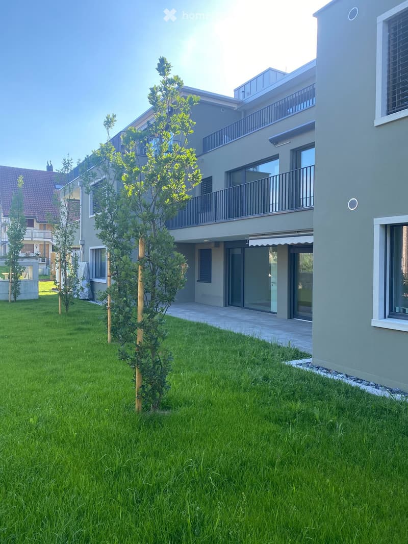 Modern apartment building with balconies, windows, sliding doors, and a courtyard with grass.