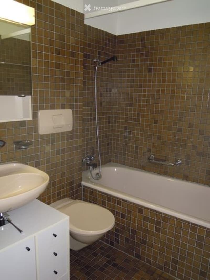 Bathroom with brown tiled walls and floor, white sink, toilet, bathtub, and showerhead.