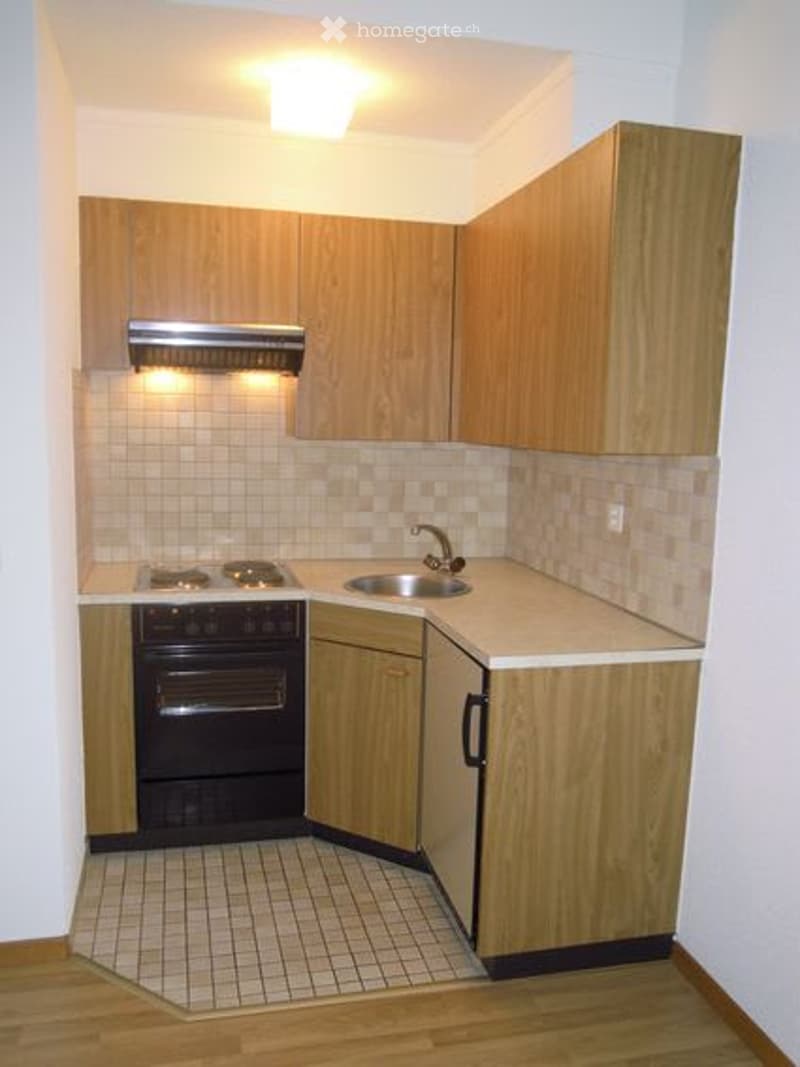Compact kitchen with wooden cabinets, a stove, oven, sink, and faucet.