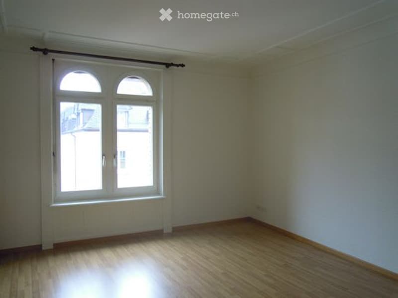 Empty room with wooden flooring, white walls, and a large arched window with a curtain rod. No furniture or equipment present.
