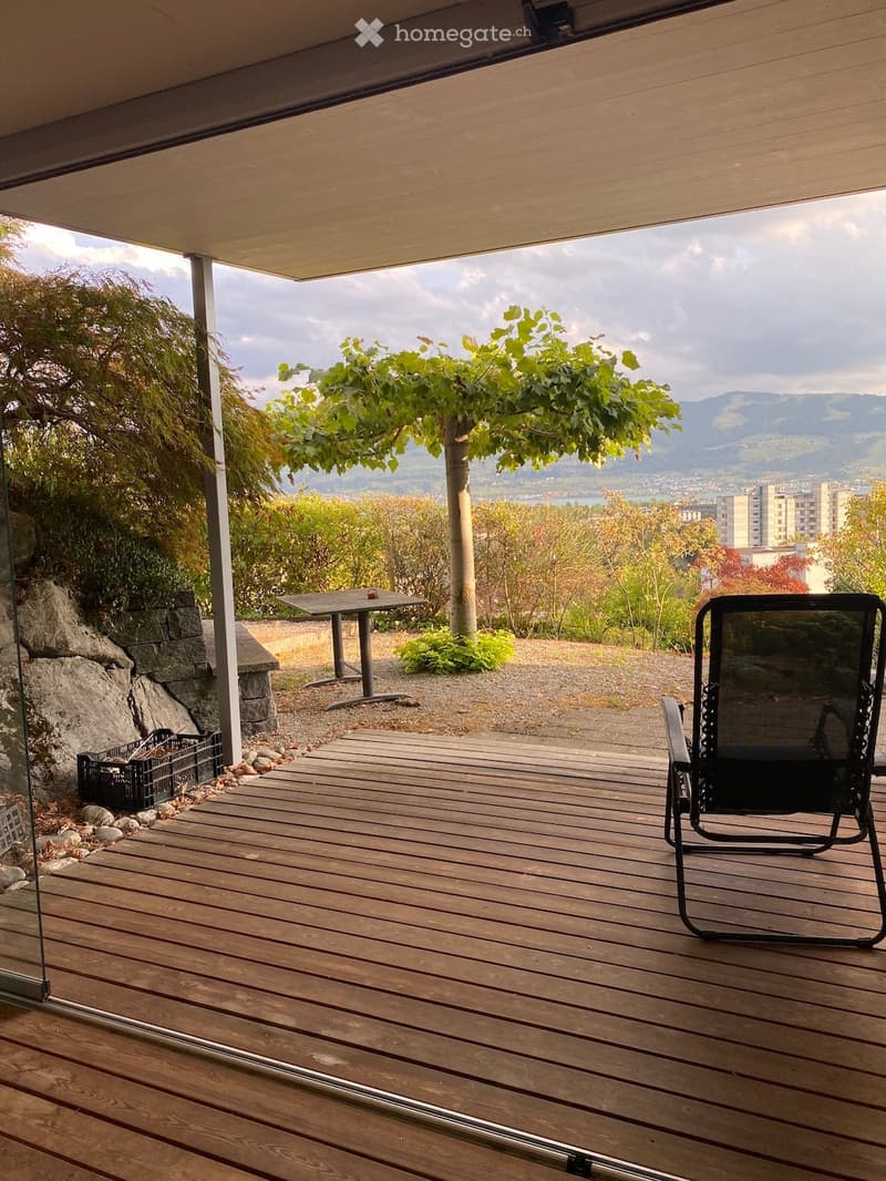 Wooden deck with a view of a landscape, featuring a black folding chair and a small table.
