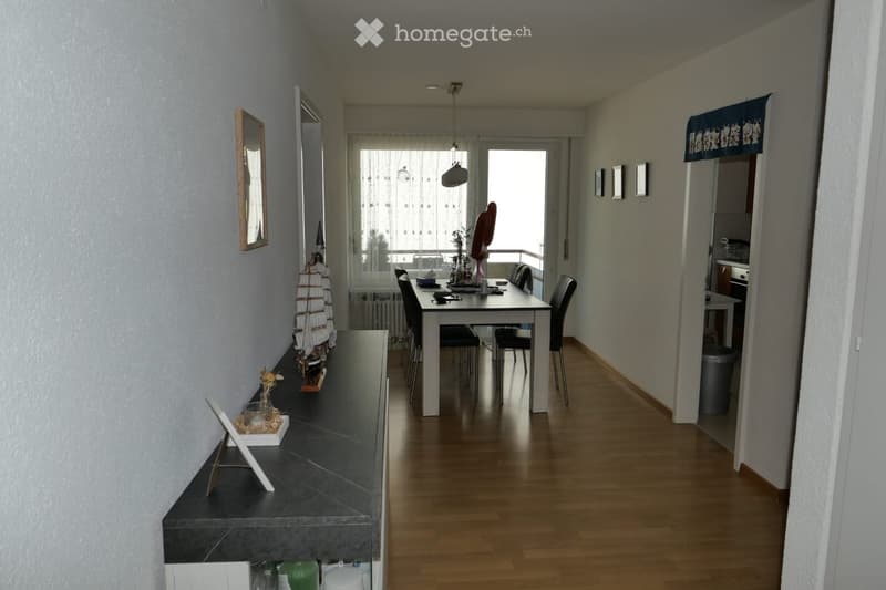 A modern hallway with wooden flooring, a dining area visible in the background, and a small decorative shelf on the left side.