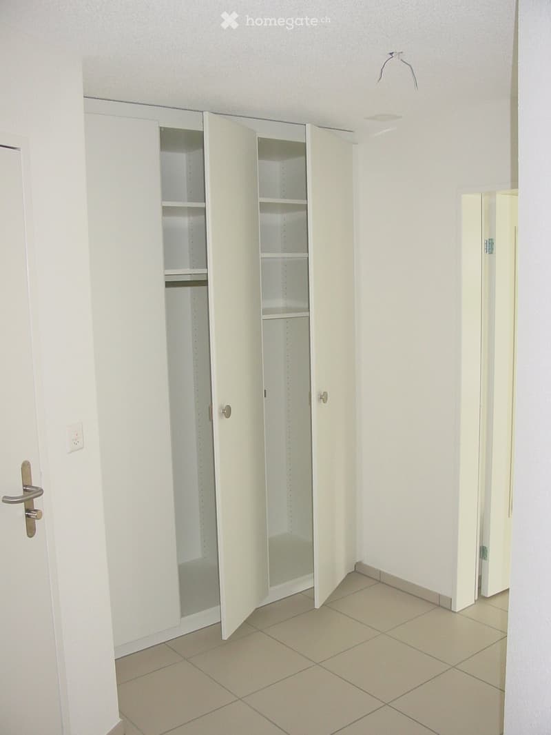 Empty room with white tiled floor, white walls, and built-in white cabinets with open doors showing empty shelves.