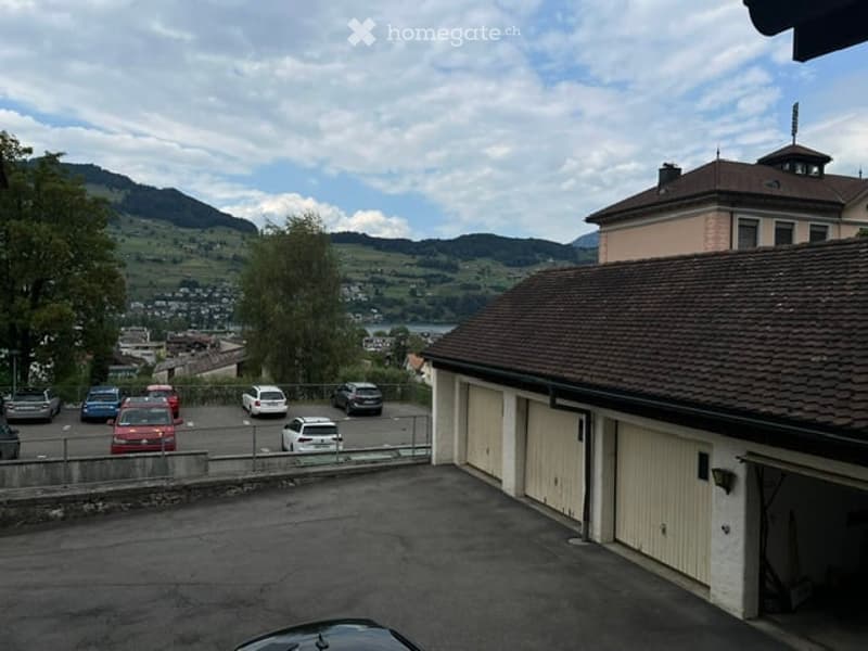 View from a rooftop showing a parking area with several cars, a garage, and a scenic mountain view in the background.